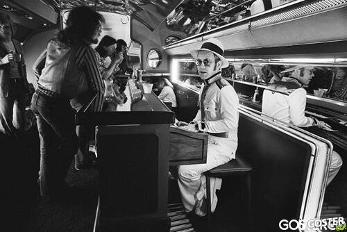 Elton John at the piano bar aboard his private plane - 1976