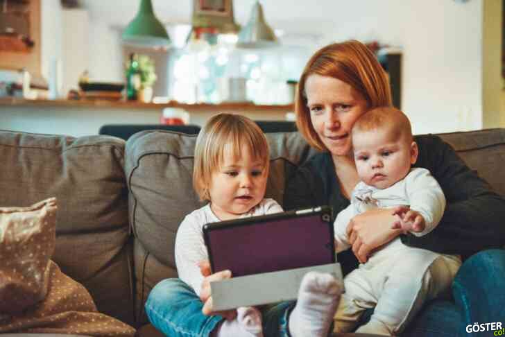 two babies and woman sitting on sofa while holding baby and watching on tablet